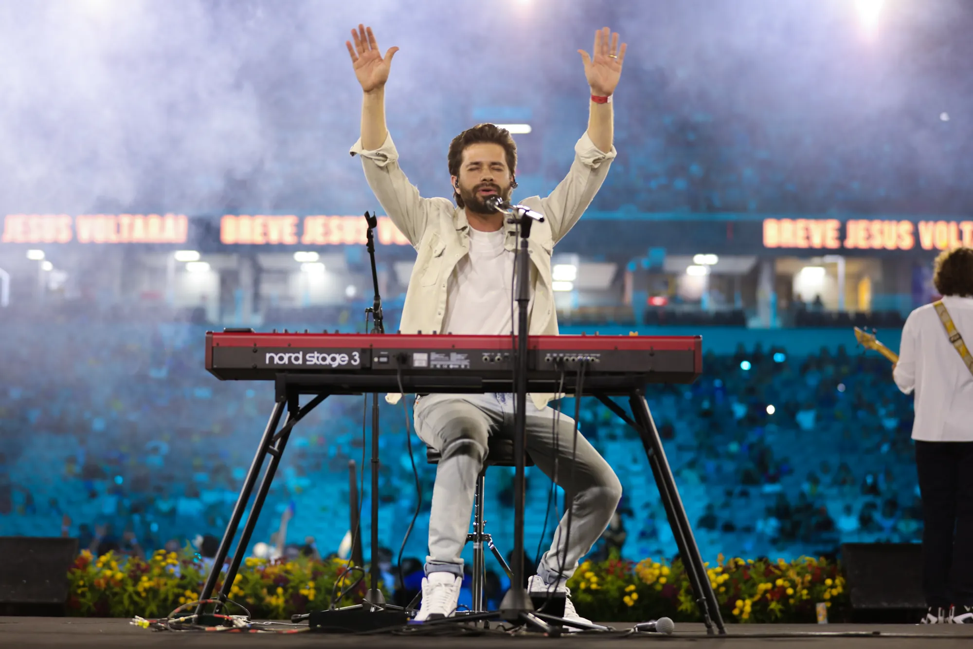 Matheus ao piano com os braços erguidos, diante de um estádio lotado