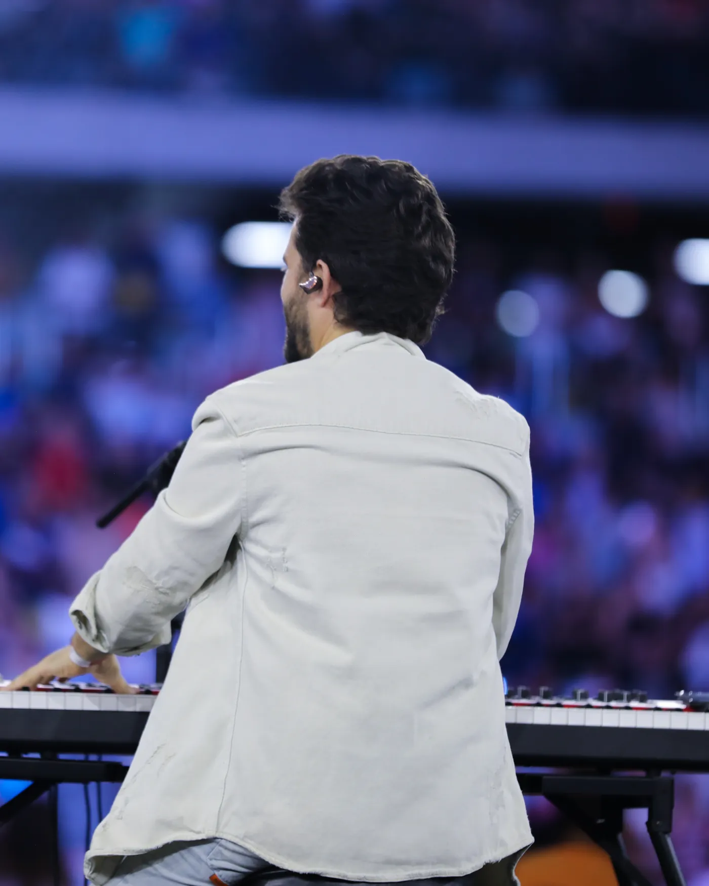 Matheus de costas, ao piano, diante da congregação num estádio